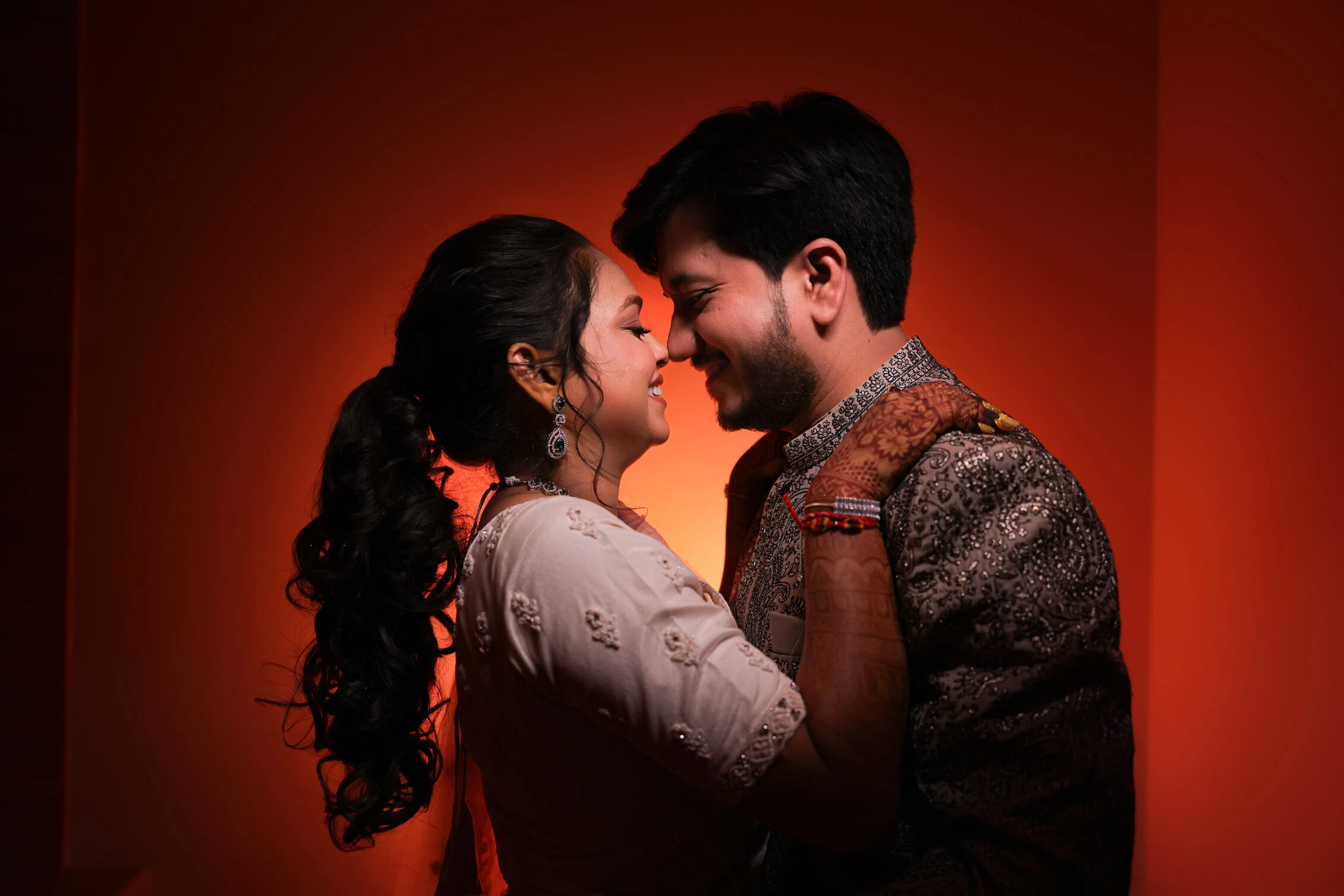Couple embracing during pre-wedding shoot with warm orange backdrop, professional wedding photography Rajkot, candid couple pose