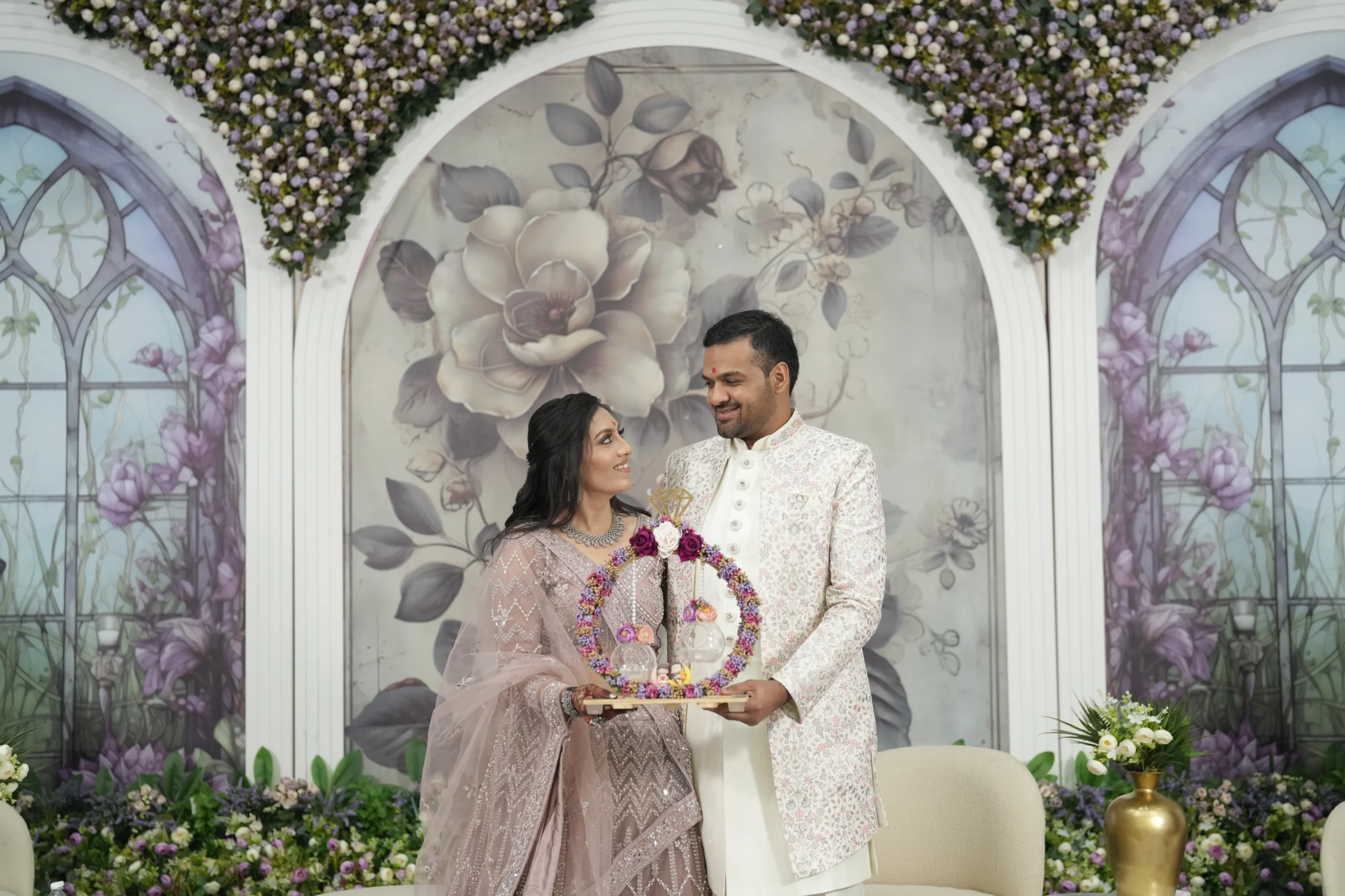 Elegant engagement ceremony in Rajkot, couple holding ring platter against floral backdrop, professional photography