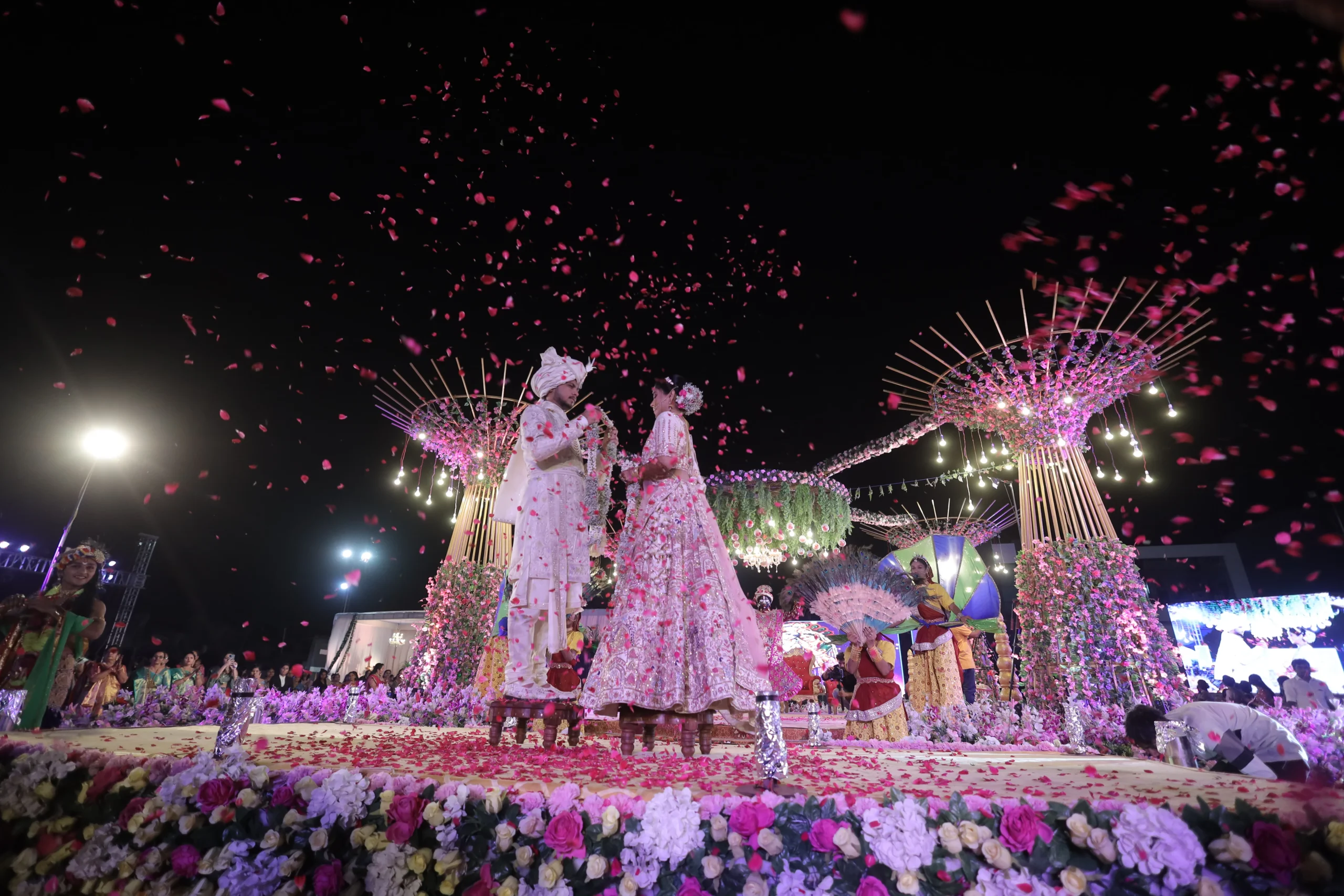 Grand Indian wedding ceremony at night, couple on floral stage with falling petals, best wedding photography Rajkot